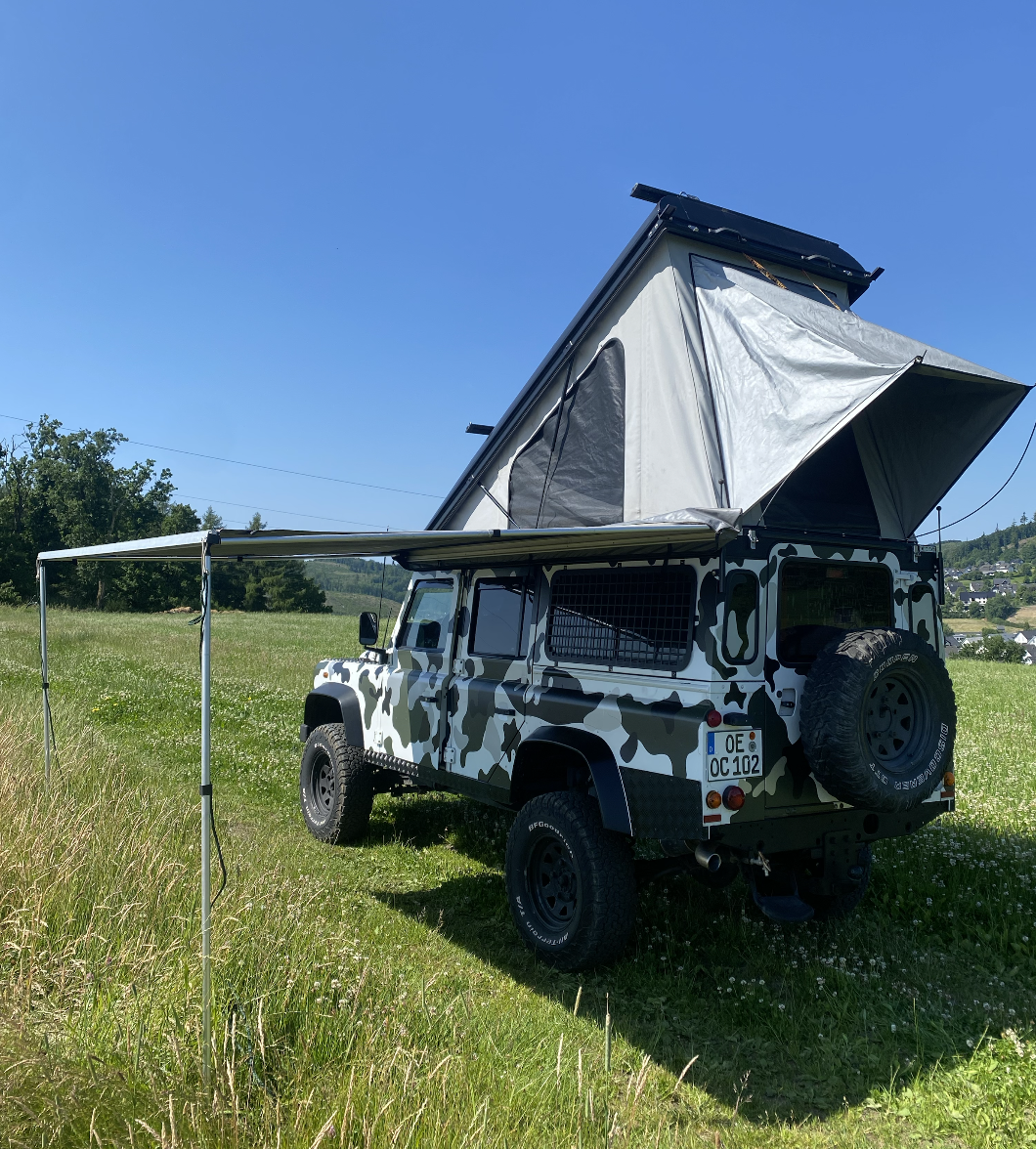 Land Rover Defender mit geöffneter Ausstattung und Aufstelldach auf einer Wiese