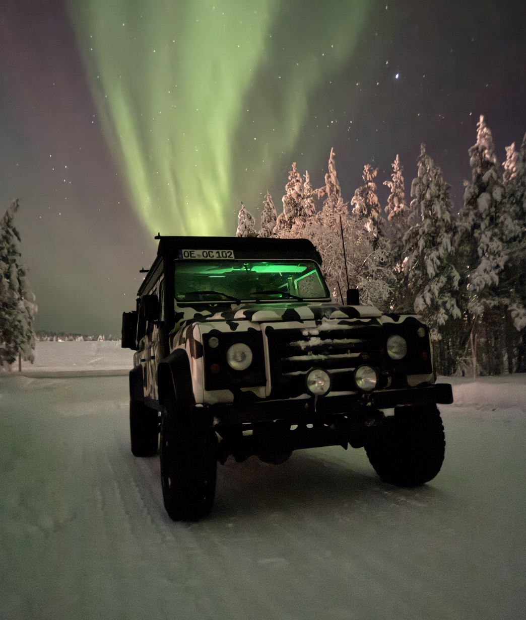 Land Rover Defender unter Polarlichtern im Schnee